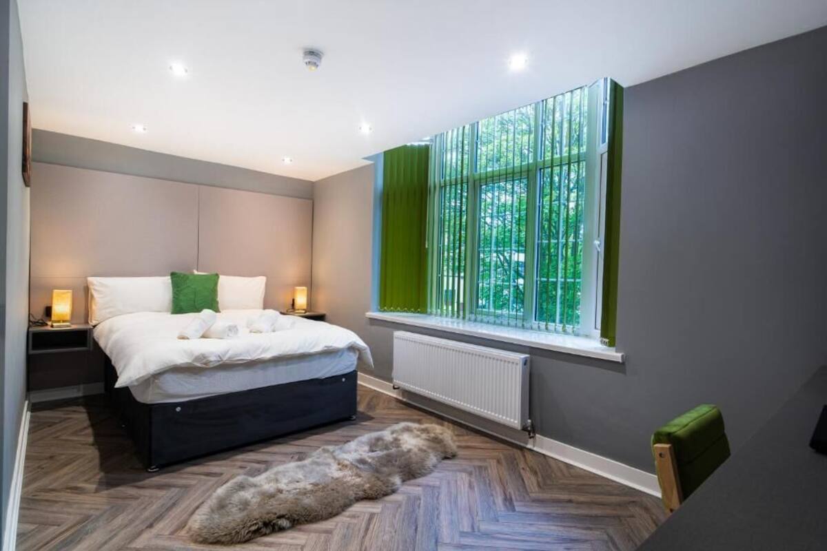 A modern bedroom with a bed, bedside lamps, a radiator, and a large window with curtains.