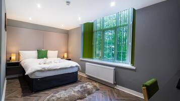 Un dormitorio moderno con cama, lámparas de noche, un radiador y un ventanal con cortinas.