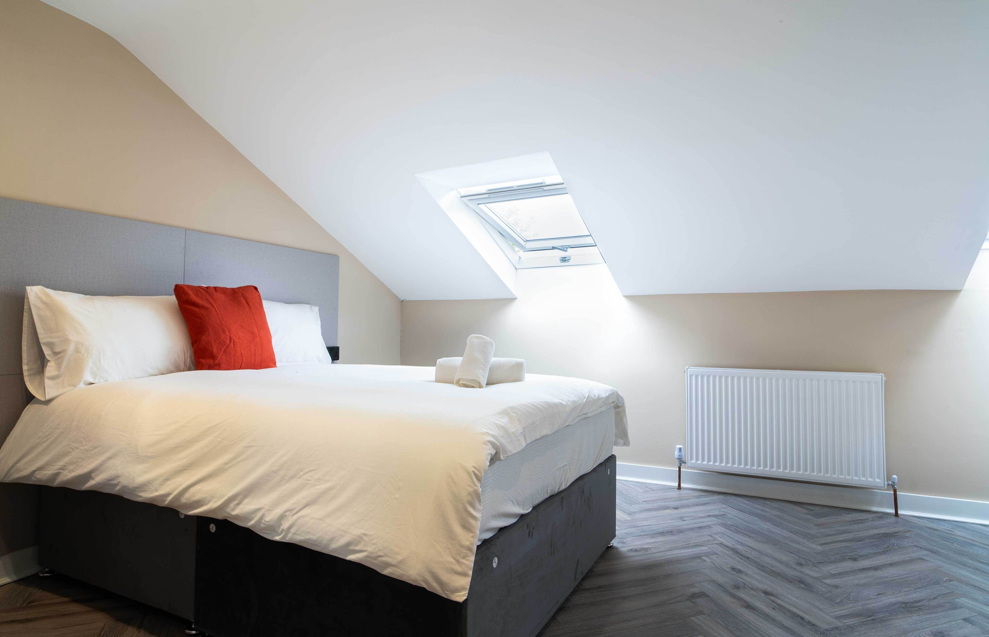 A bedroom with a bed, a skylight, a radiator, and a herringbone-patterned floor.