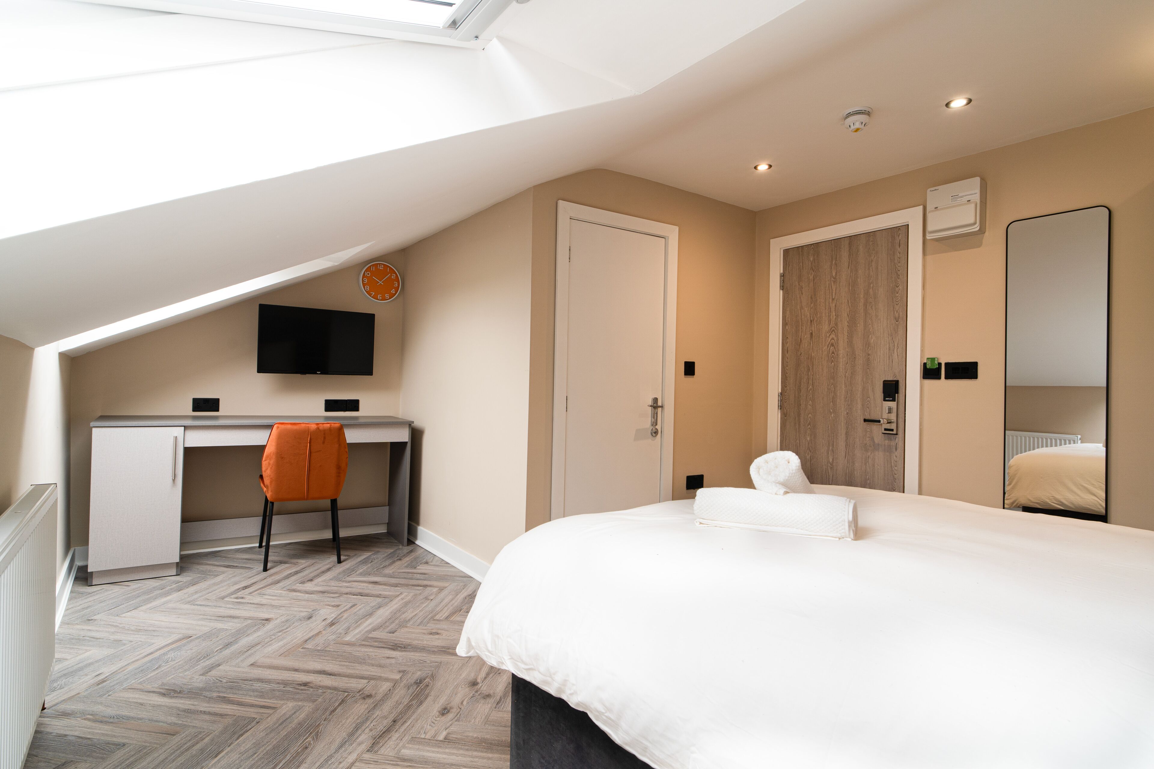 A modern hotel room with a loft-style ceiling, a bed, a desk, and a chair.