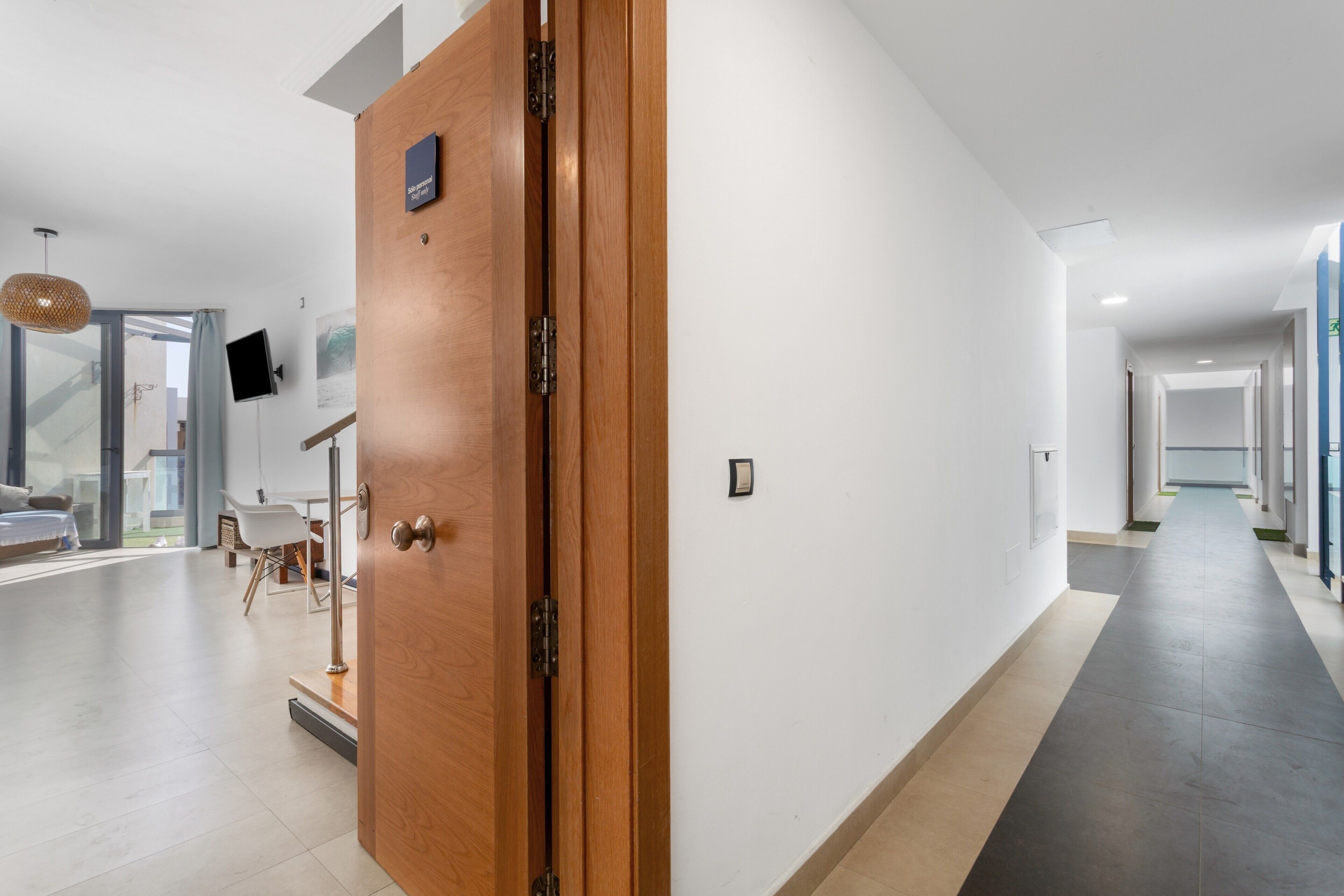 Ein moderner Hotelkorridor mit einer Holztür, einem an der Wand befestigten Flachbildfernseher und einer Treppe, die zu einer anderen Ebene führt.