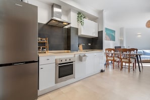 Ett modernt kök med vitvaror i rostfritt stål, vita köksluckor och en matplats med trästolar.