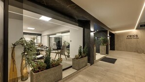 A modern hotel lobby with a glass wall, indoor plants, and a sign for 'CENS Luxury Suites'. - Gold Suites (Ioannina)