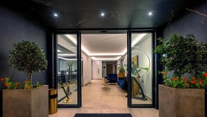 Ein moderner Hotelzugang mit Glastüren, einer Rezeption und Zimmerpflanzen.
