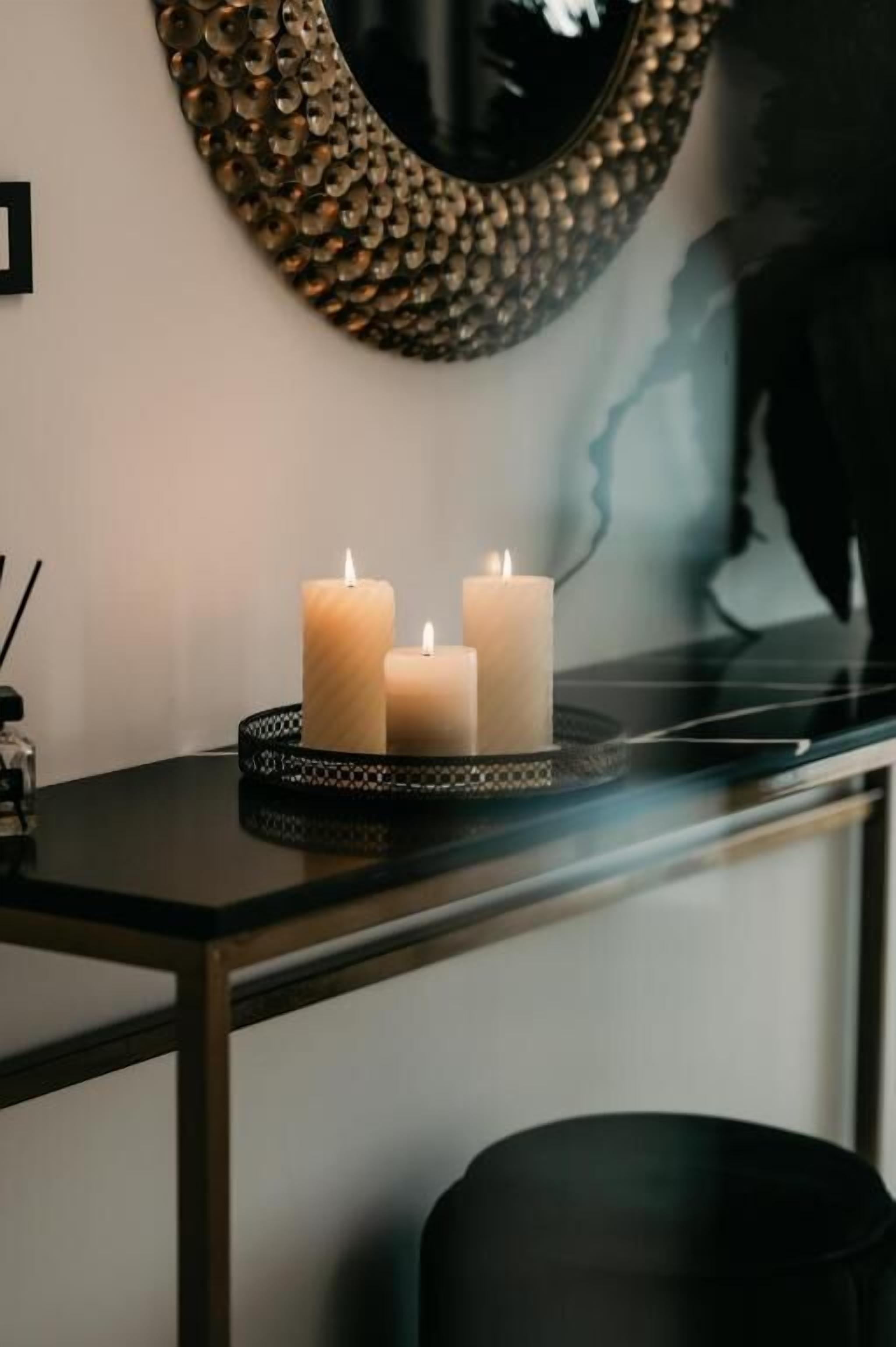 A modern interior with a decorative mirror, three lit candles on a tray, and a silhouette artwork on the wall.