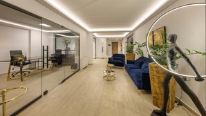 A modern office space with glass walls, a blue sofa, and a treadmill. - Gold Suites (Ioannina)
