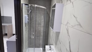 A modern bathroom with a glass shower enclosure, a sink with a mirror, and marble-tiled walls. - 1066 Apart Hotel (Hastings)