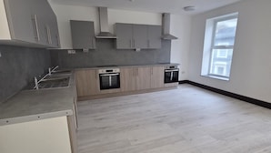 A spacious kitchen with grey cabinets, a central island, and a large window providing natural light. - 1066 Apart Hotel (Hastings)