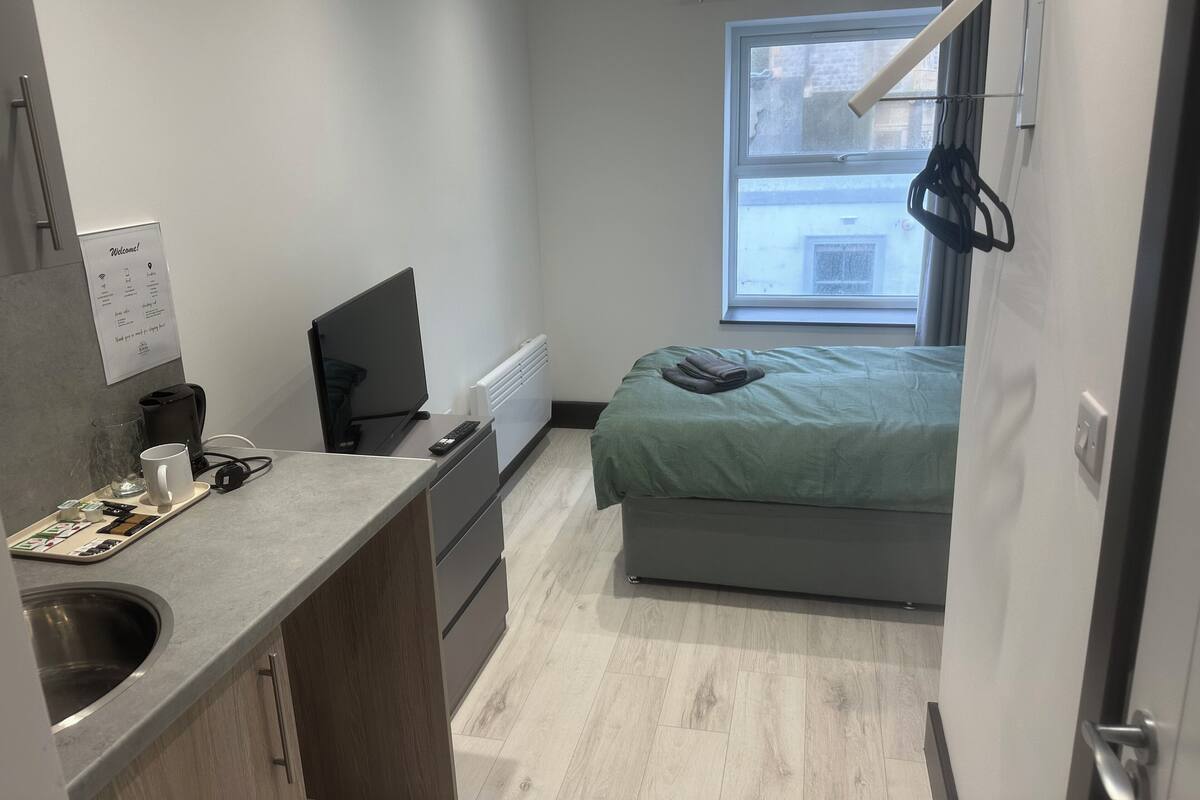 Habitación de hotel compacta con kitchenette, cama, ventana con vistas y una puerta.