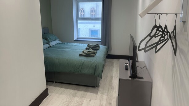 A modern bedroom with a bed, a window, a flat-screen TV, and a wall-mounted coat rack. - 1066 Apart Hotel (Hastings)