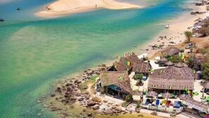 Un hotel frente al mar con acceso a la playa, estructuras de techo de paja e insignias que señalan una ubicación caribeña.