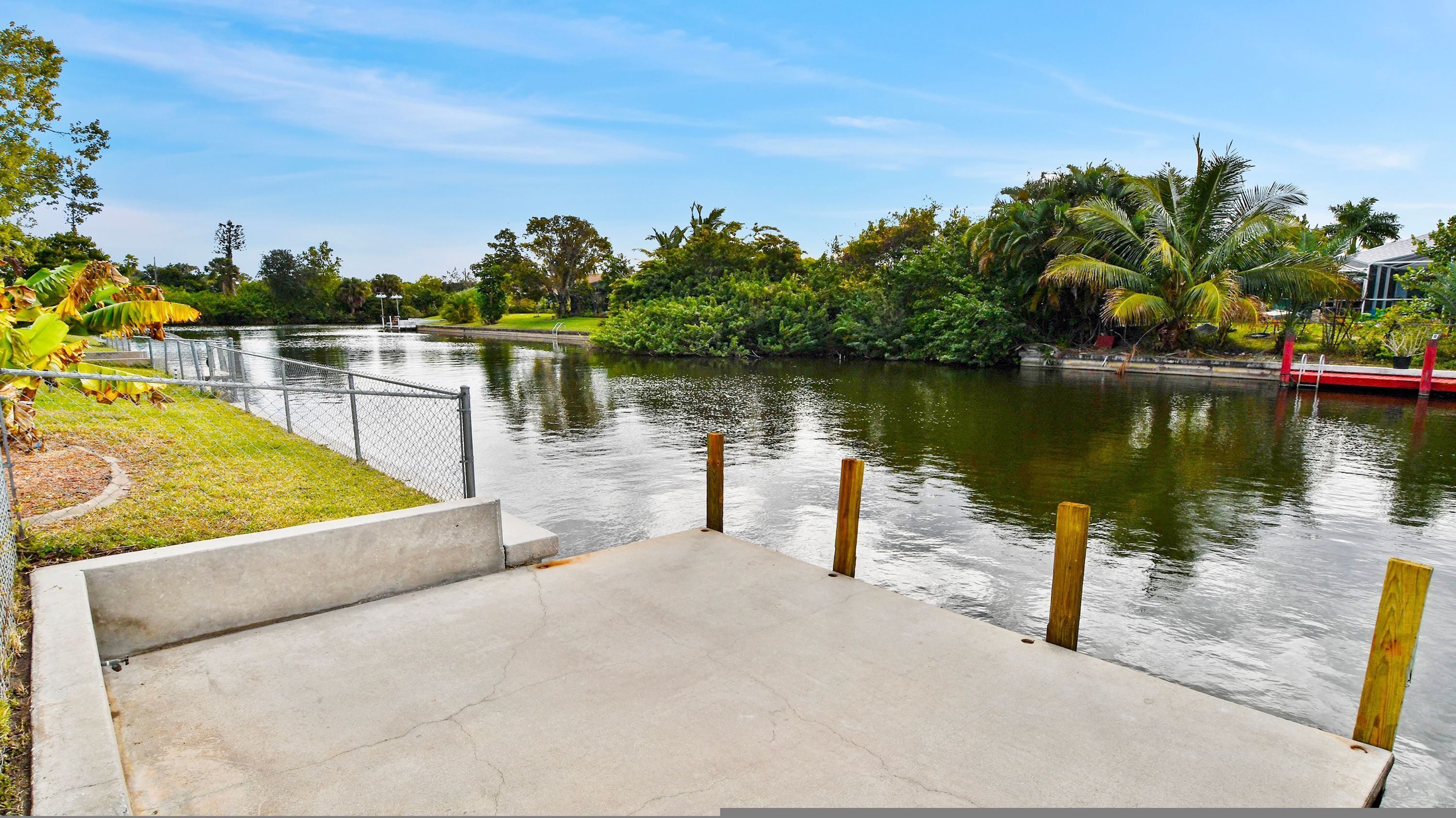 A concrete staircase leading to a dock over a calm river, surrounded by lush greenery and a clear sky.