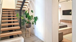 Eine moderne Treppe mit Holzdielen und einem Metallgeländer, die zu einem Zimmer mit einem Bett und einem Flachbildfernseher führt.