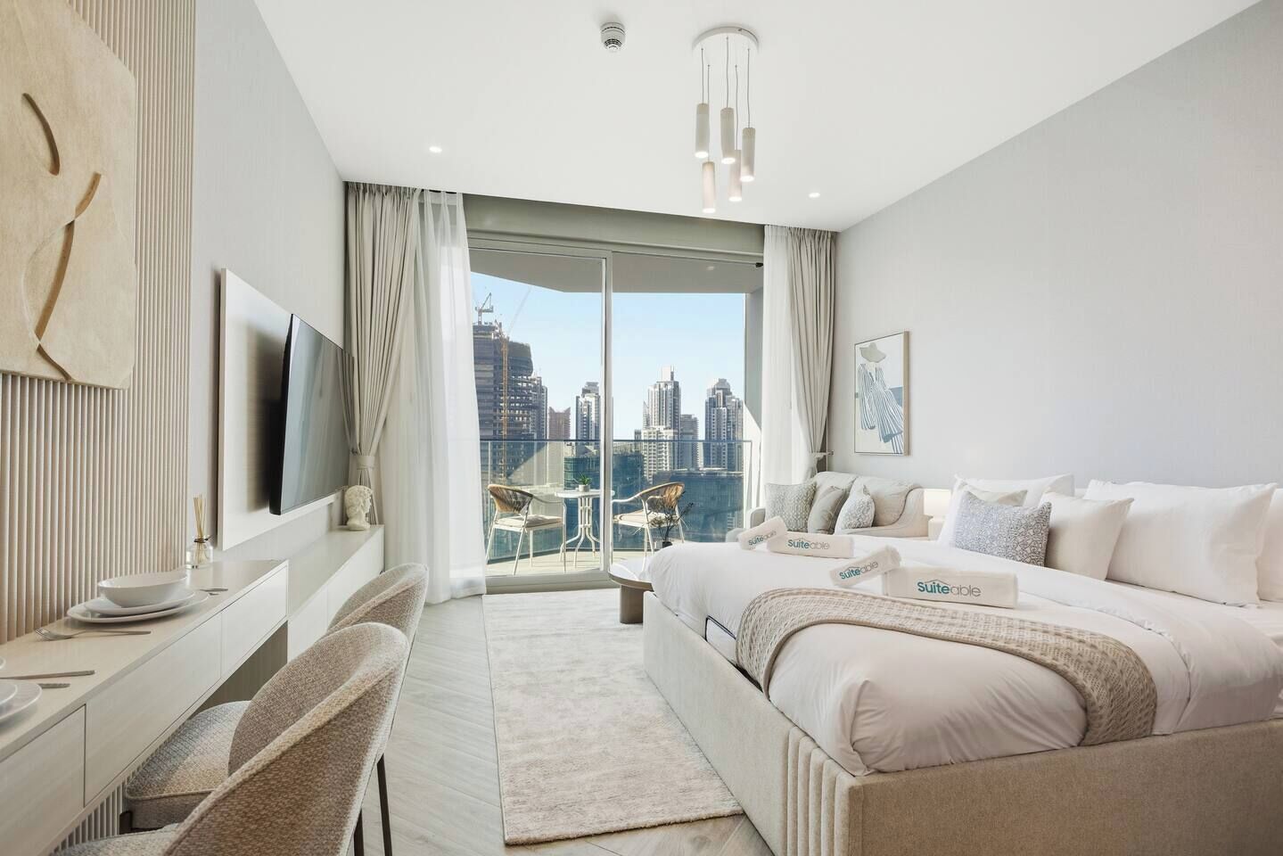 Quarto de hotel moderno com uma cama grande, uma escrivaninha com cadeira, televisão e varanda com vista para a cidade.