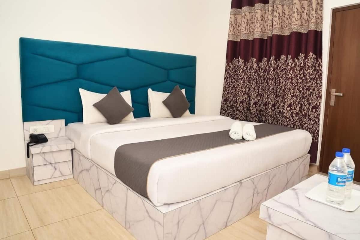 Una habitación de hotel con un cabecero color turquesa, una cama con estampado de mármol, una mesita de noche con un teléfono y una mesita auxiliar.
