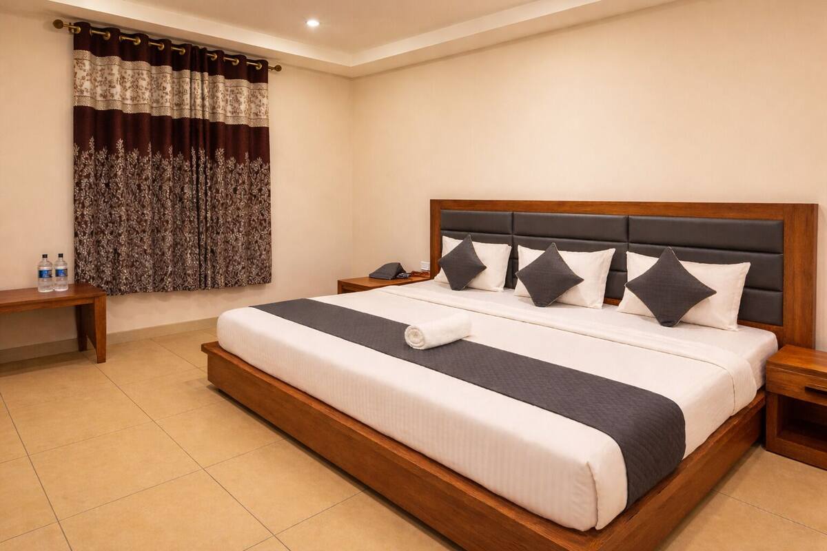 Una habitación de hotel con una cama grande, cabecera de madera, una mesita de noche y una cortina con estampado floral.