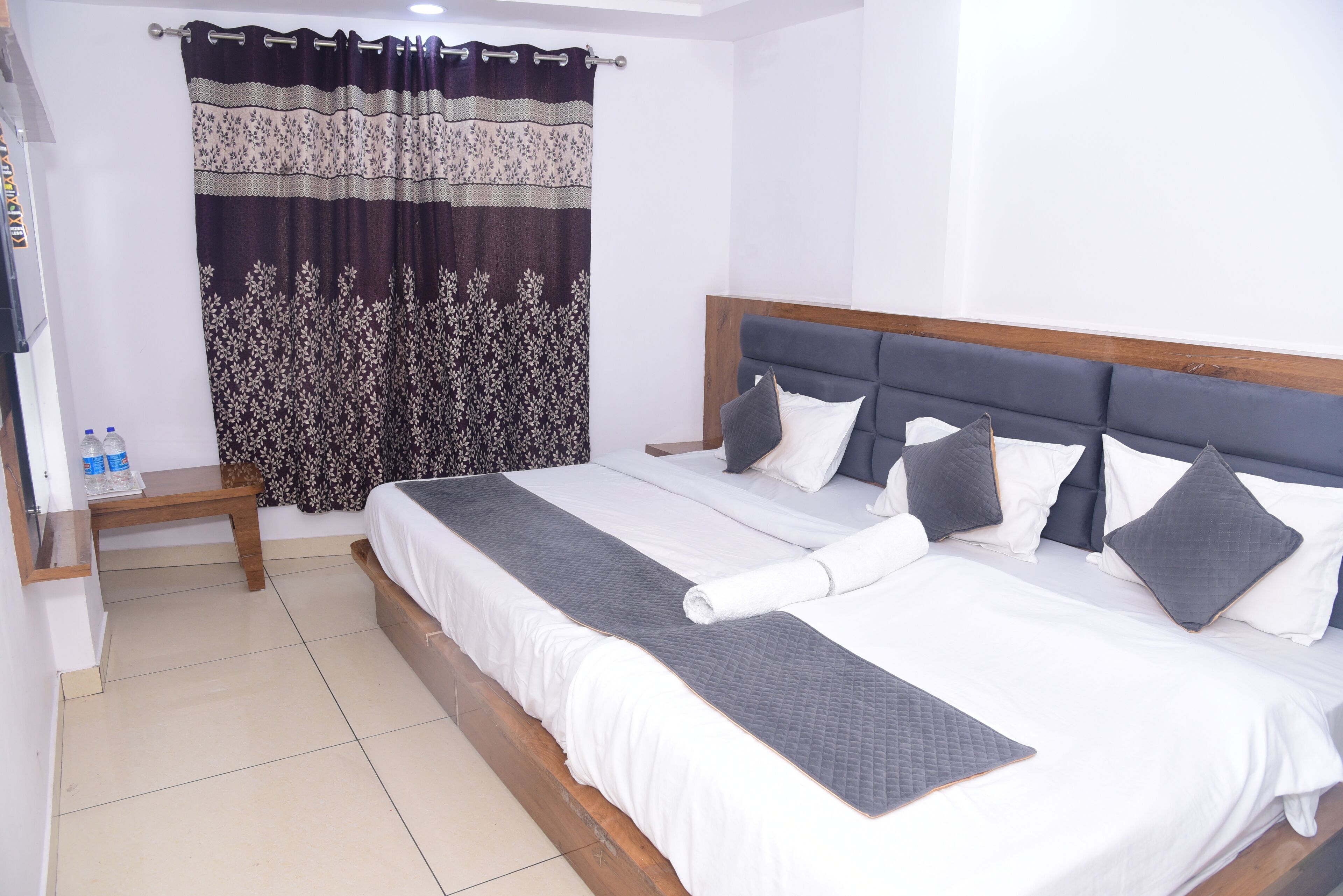 A neatly made bed with a headboard, a wooden bench, and a curtain with a floral pattern.