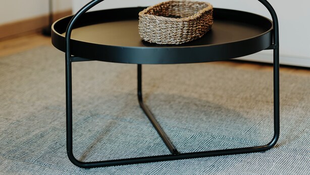 A modern room with a round black metal table, a woven basket on it, and a sofa with a yellow and patterned pillow in the background. - Cosy house in Volvic - Calm, nature & volcanoes (Volvic)