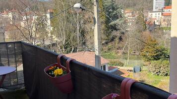 Un balcon avec deux jardinières contenant des fleurs jaunes, une table et une vue sur des bâtiments et des arbres en arrière-plan.