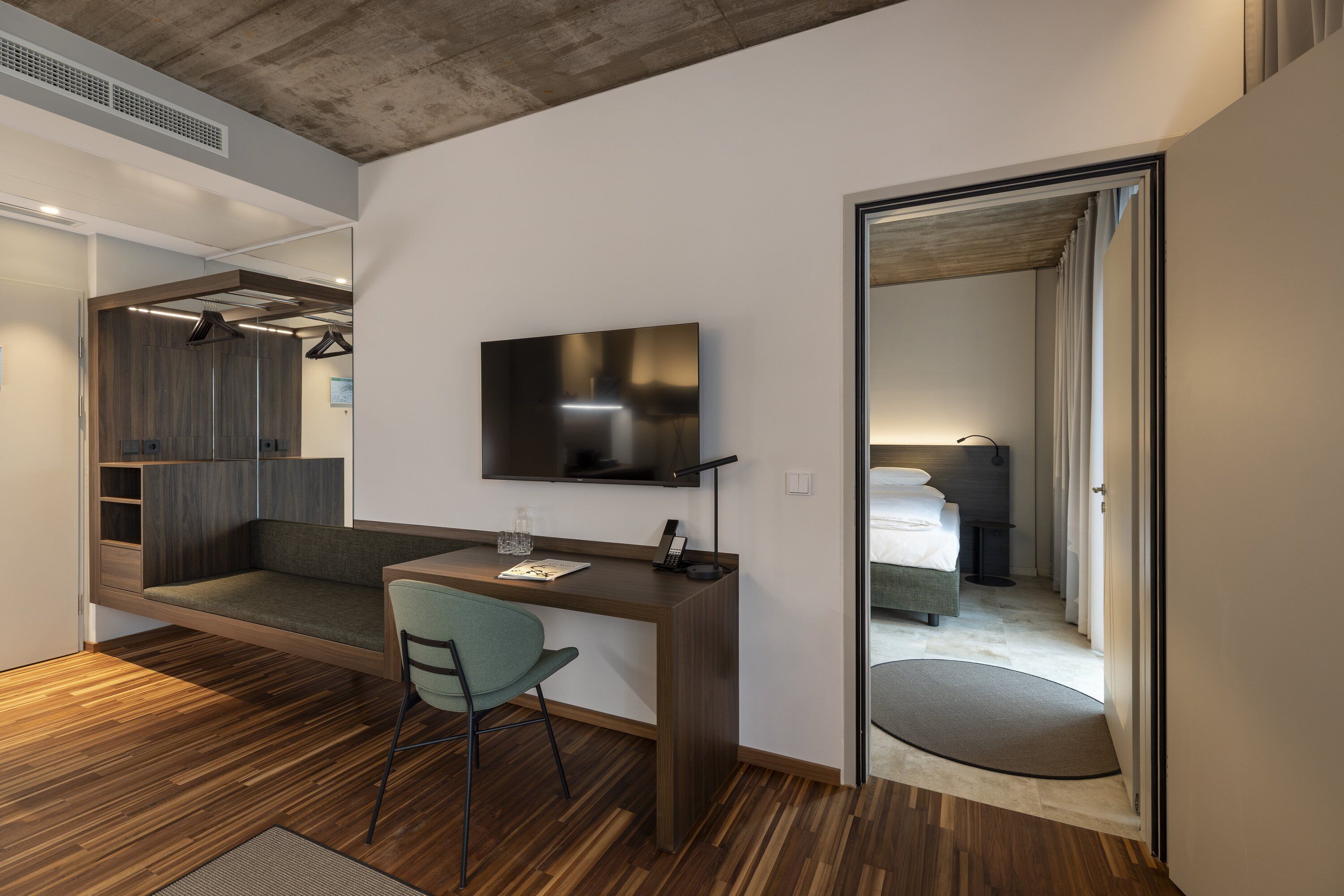 Una habitación moderna con un escritorio de madera, una silla, un televisor de pantalla plana y una cama con cortinas.