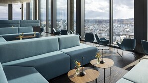 Un salon moderne doté d’un canapé, de fauteuils et de tables rondes, et offrant de grandes fenêtres avec vue sur la ville.