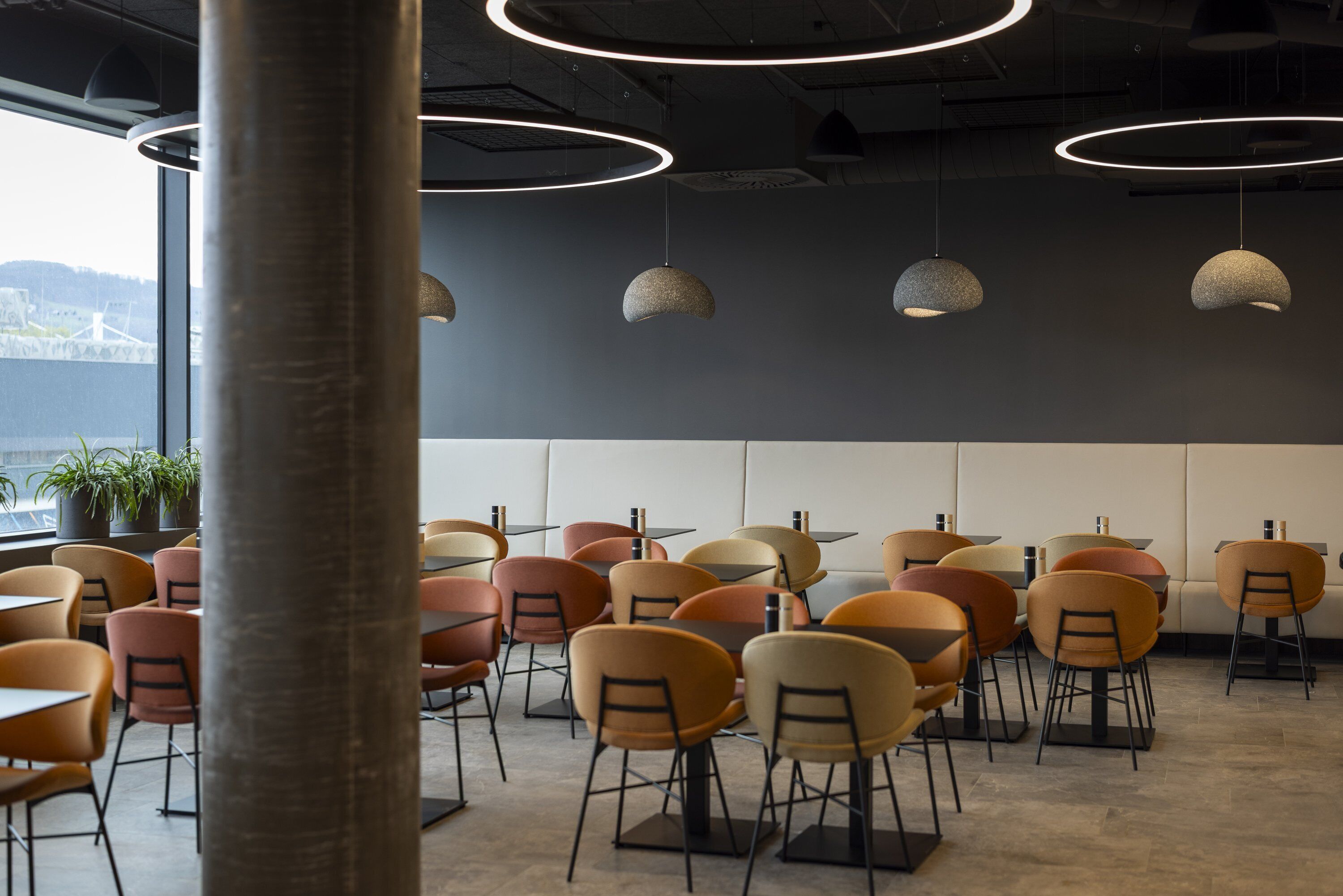 Un comedor moderno con mesas y sillas redondas, iluminación colgante y vista a un puente.