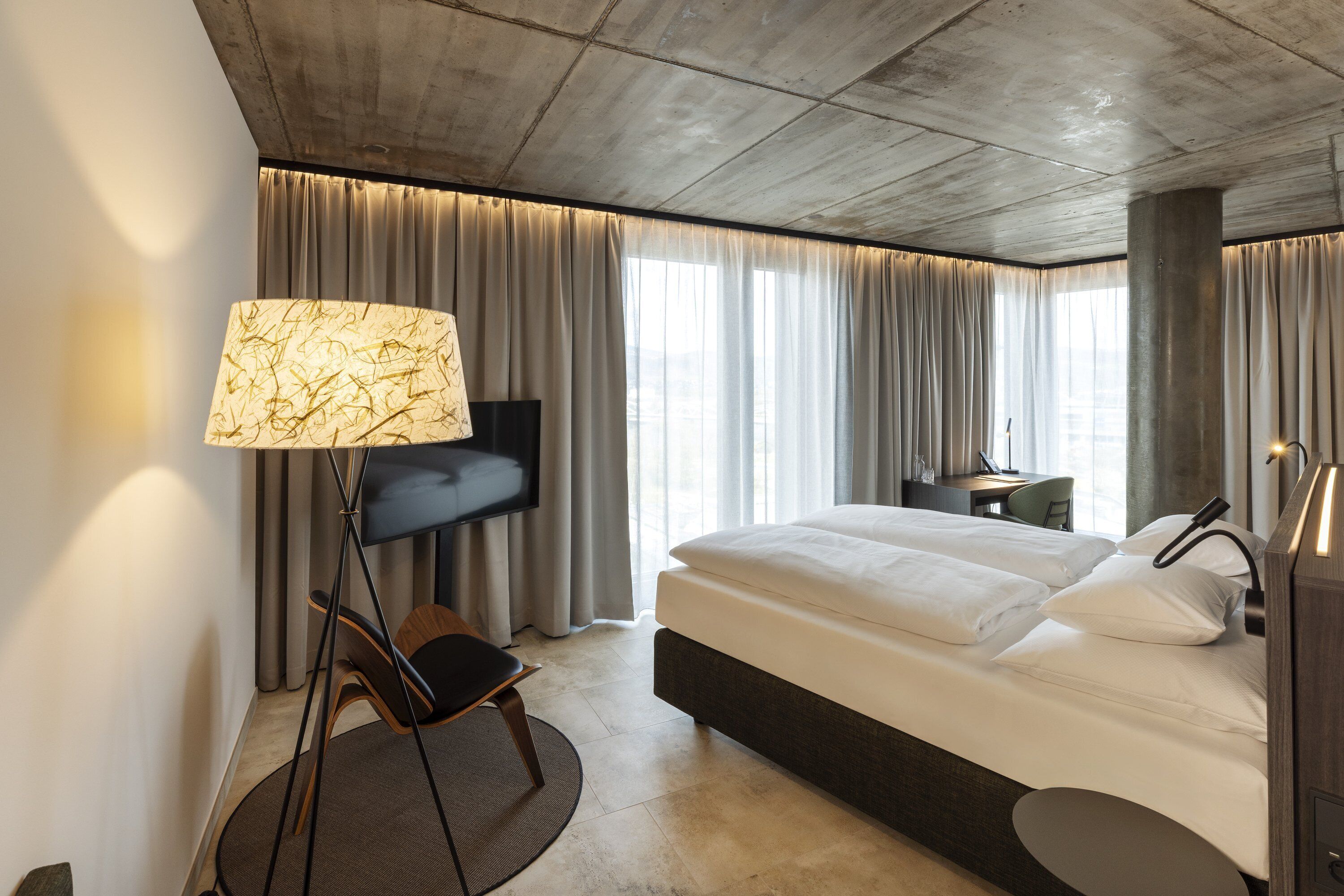 Habitación de hotel moderna con una cama grande, un escritorio, una silla, un televisor y una lámpara.