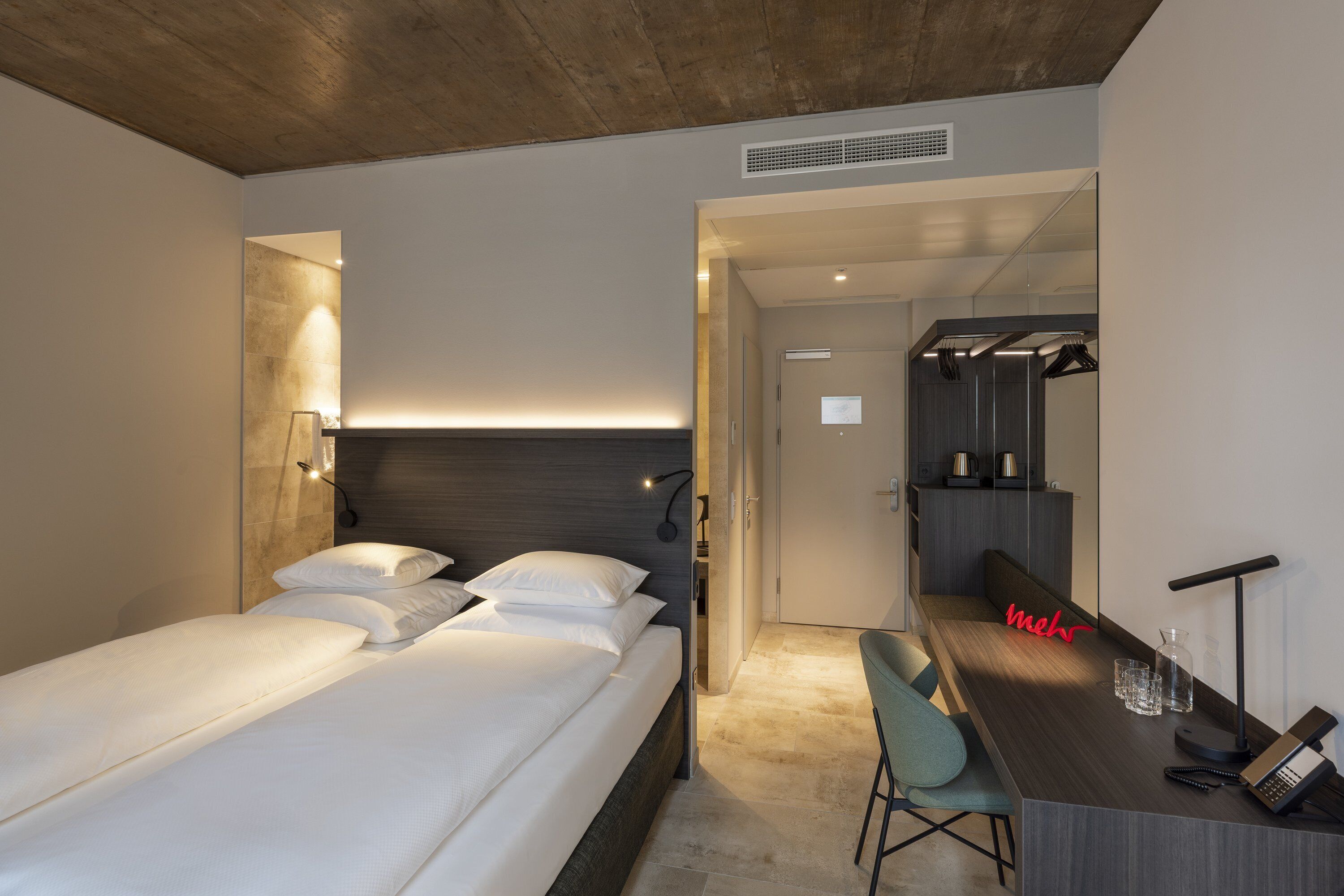 Una habitación de hotel moderna con cama, mesita de noche, silla y escritorio con espejo y teléfono.