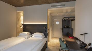 Una habitación de hotel moderna con cama, mesita de noche, silla y escritorio con espejo y teléfono.