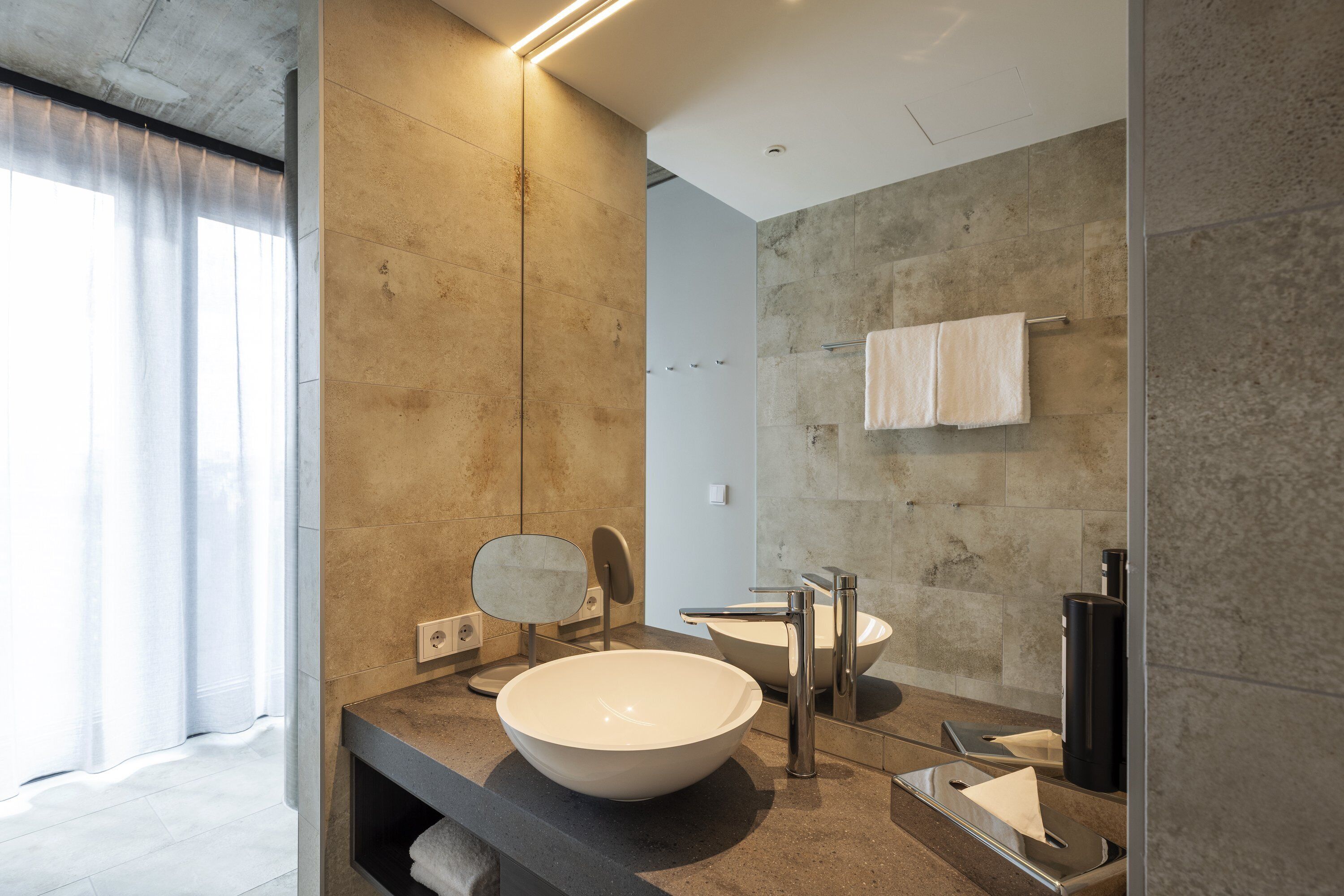 A modern bathroom with a large bowl sink, a mirror, a towel rack, and a shower area.