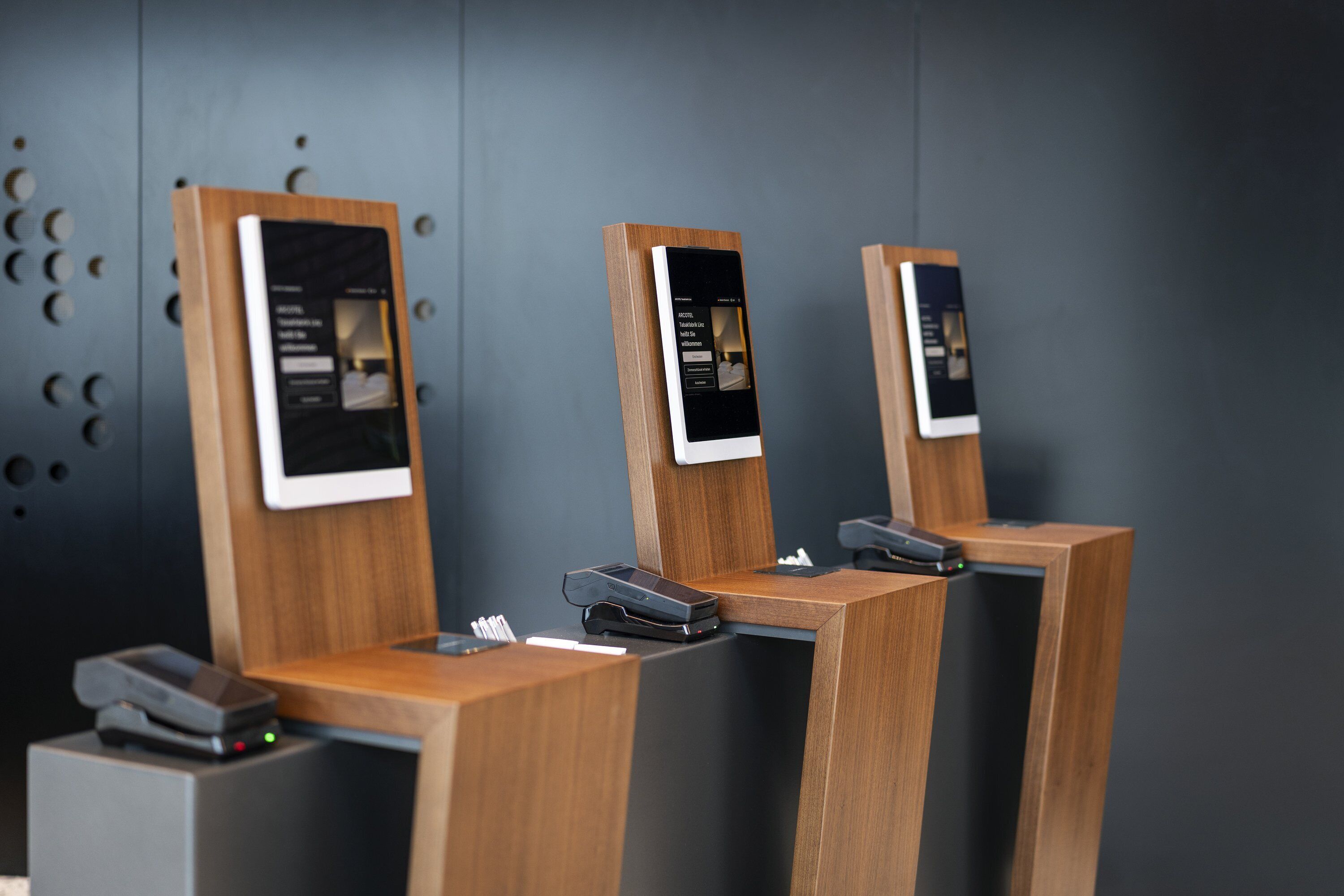 Three reception desks with digital displays, a printer, and a small table with a phone and papers.