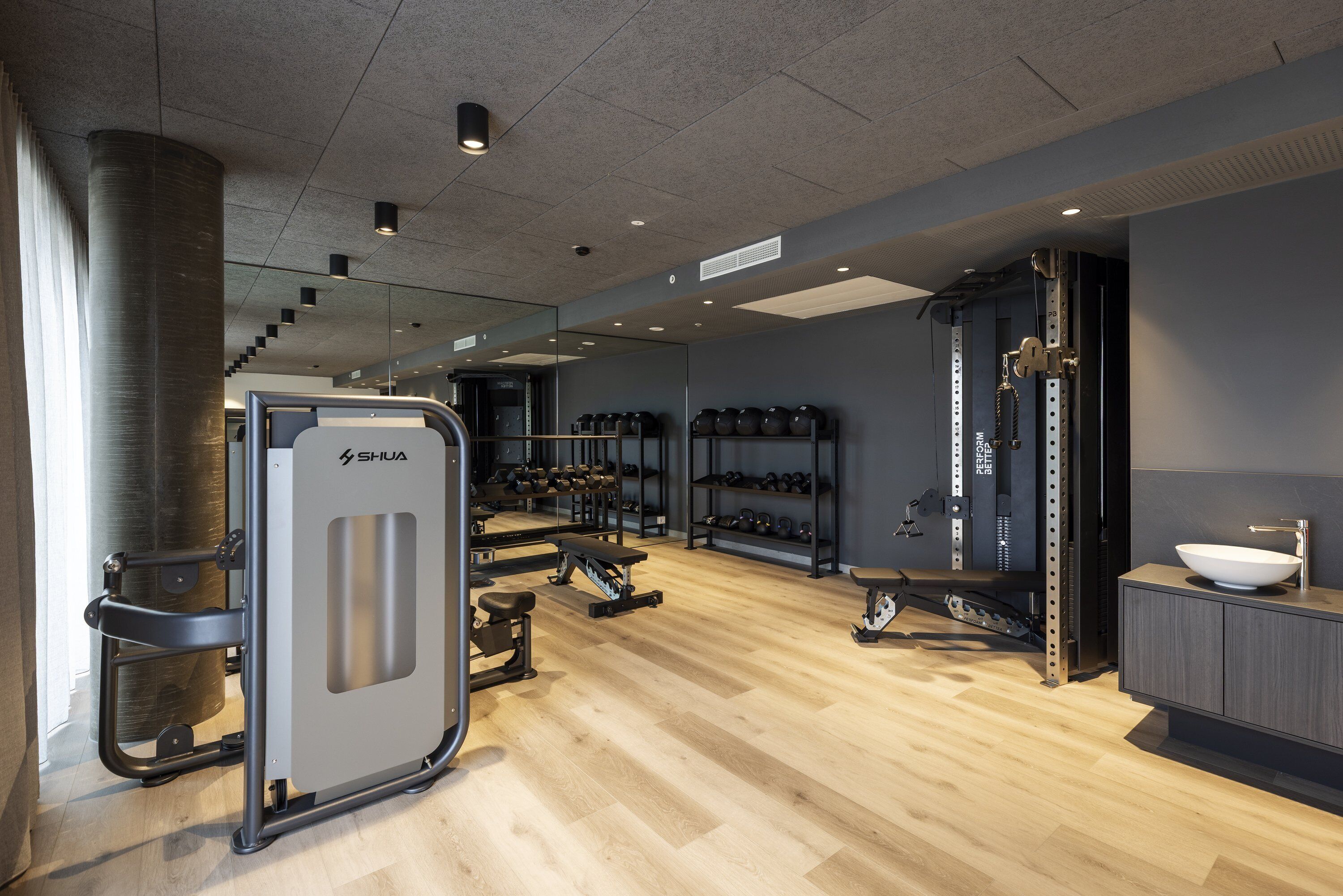 Ein modernes Fitnessstudio mit Trainingsgeräten, einer Spiegelwand und Holzboden.