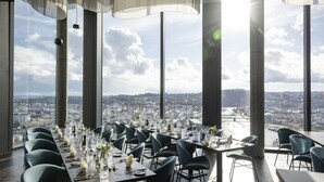 Un espace repas avec des tables dressées pour le service, de grandes fenêtres offrant une vue sur la ville et des chaises modernes.