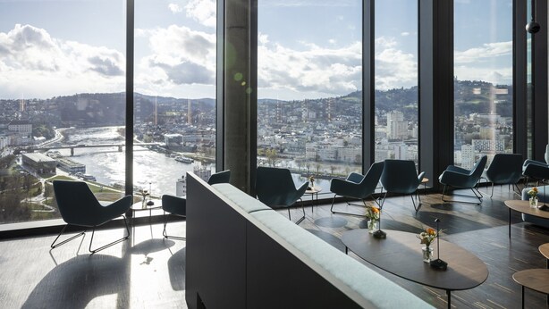Un intérieur moderne avec de grandes fenêtres, un coin salon et une vue sur le paysage urbain.