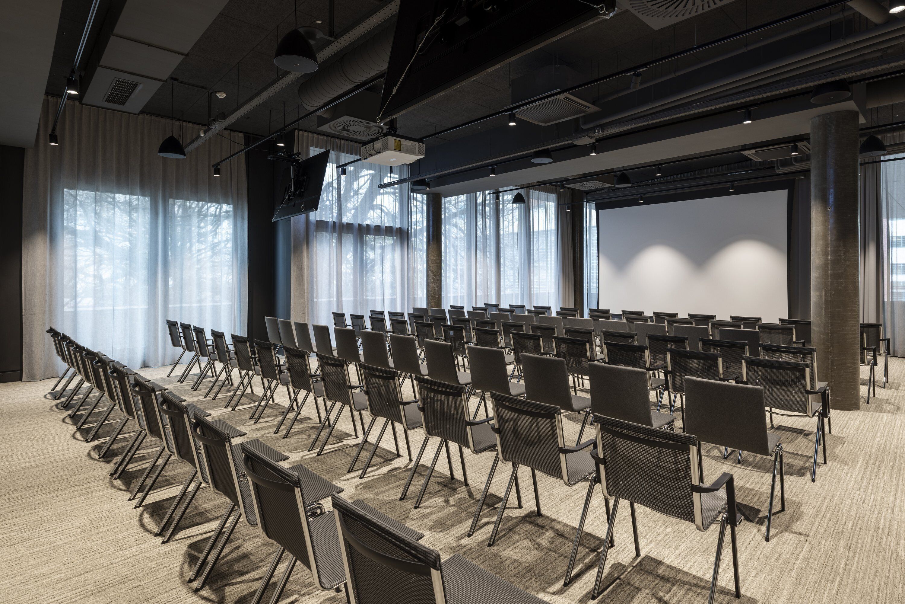 A conference room with rows of chairs, a large screen, and a projector.