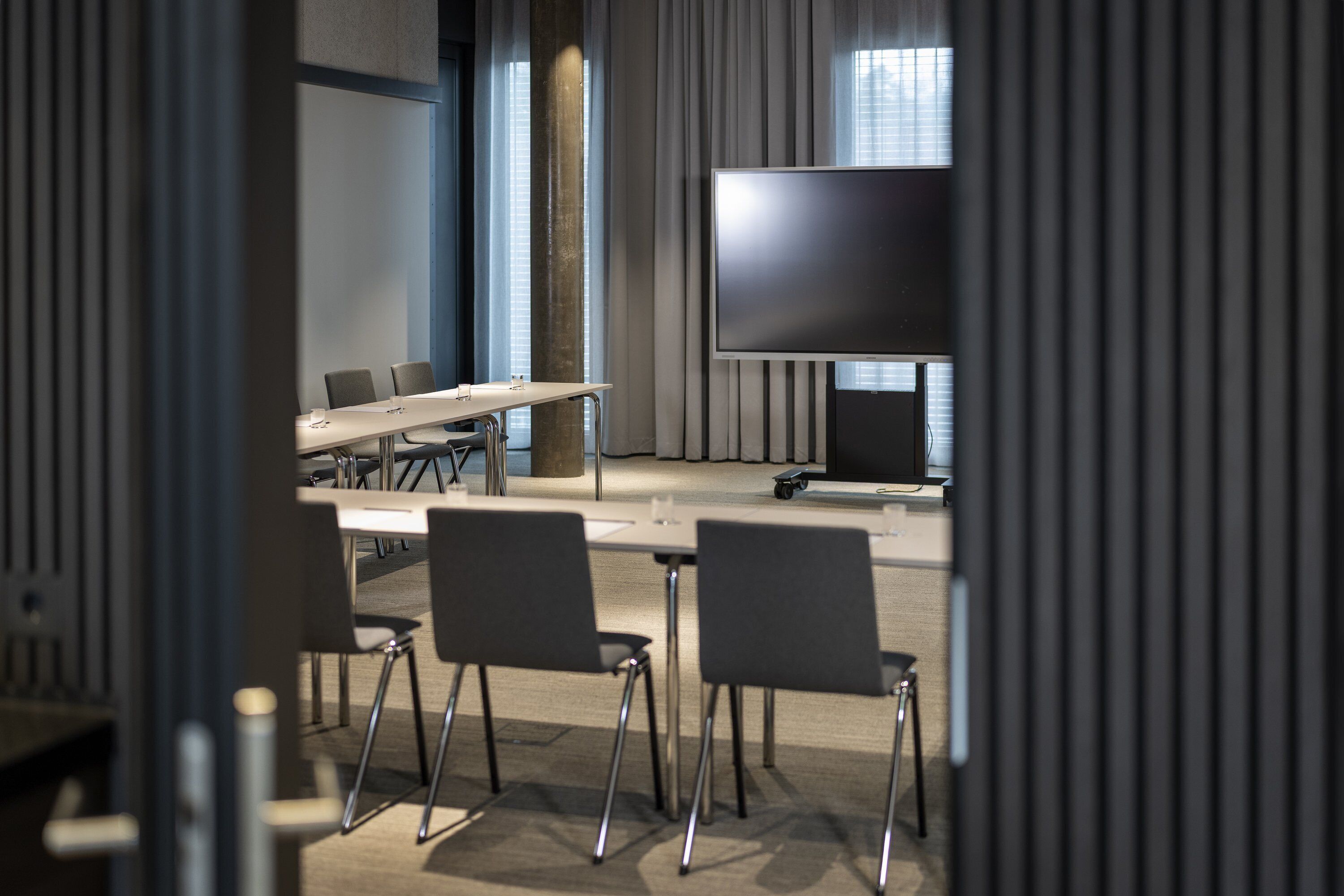 A conference room with a large flat-screen TV, a long table with chairs, and a projector.