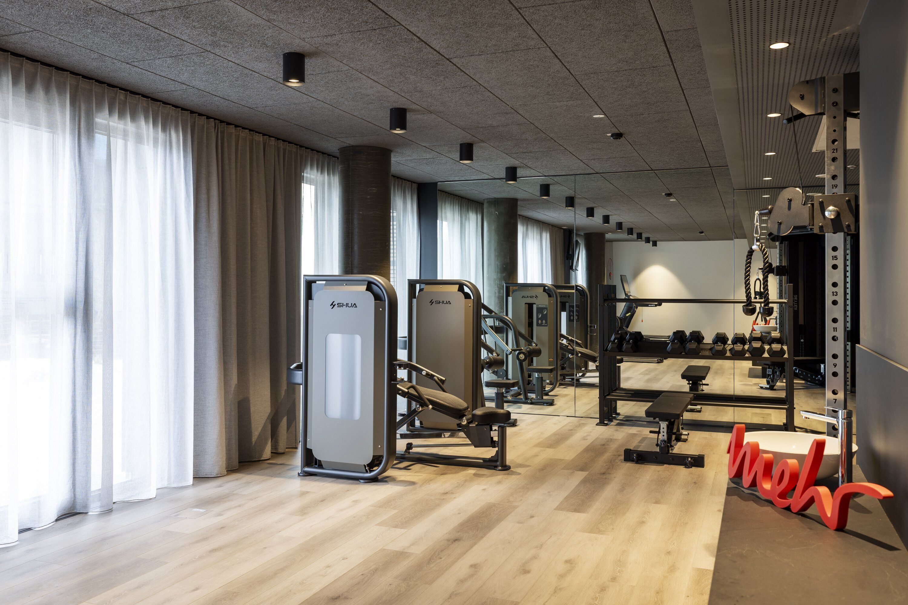 Un gimnasio con equipo de ejercicio, espejos y suelo de madera.