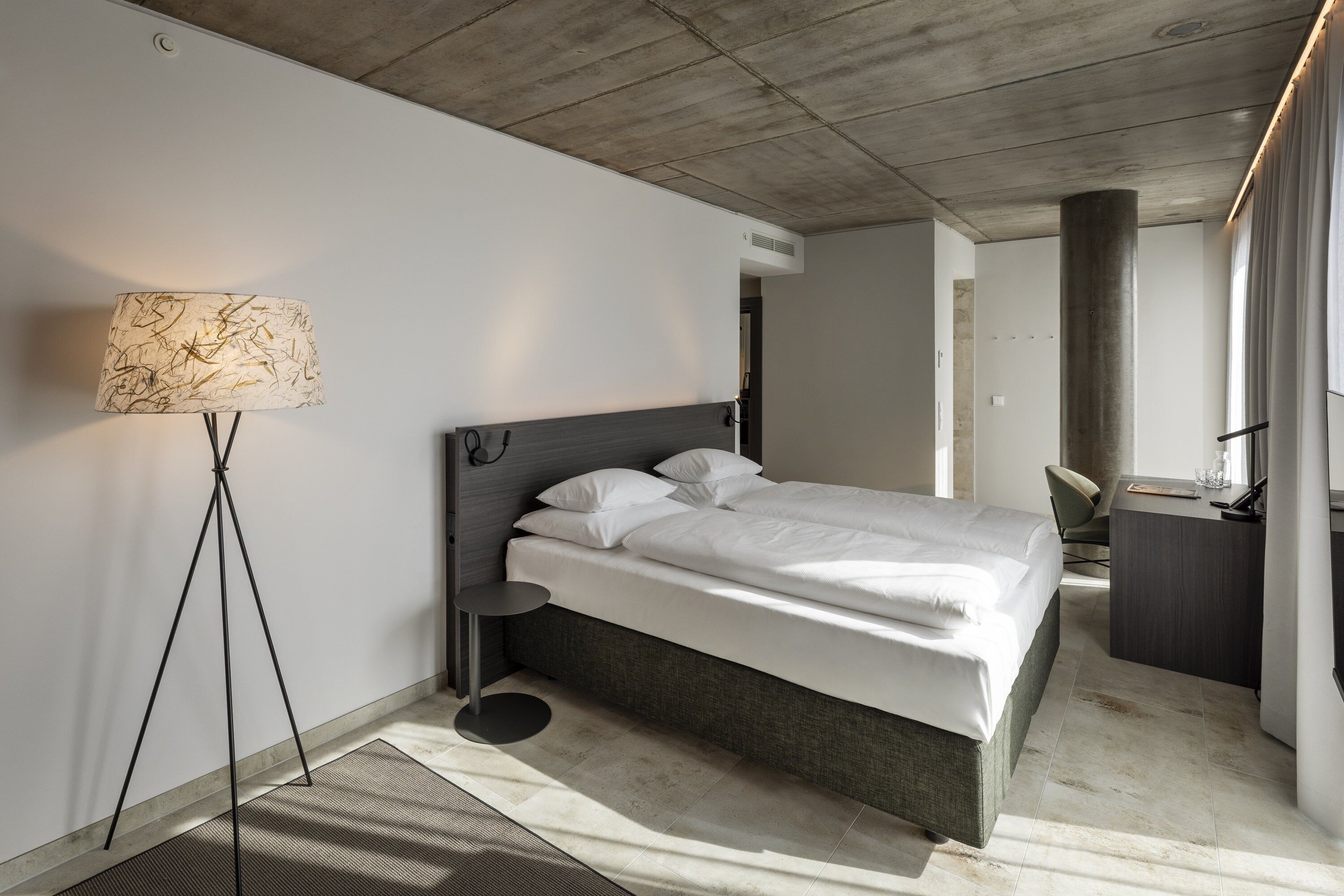 Una habitación de hotel moderna con una cama, una lámpara de pie, un escritorio y una silla.