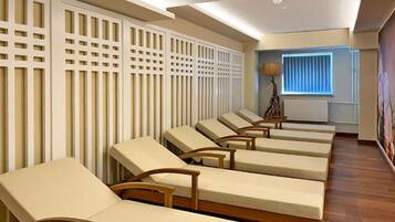 A room with multiple reclining chairs aligned against a wall with a lattice design, a window with blinds, and a lamp.