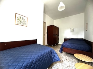 Een kamer met twee bedden, een houten garderobe, een tafeltje en een plafondlamp.
