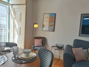 Ein modernes Wohnzimmer mit Essbereich, ausgestattet mit einer Couch, Sesseln, einem kleinen Tisch und einer Stehlampe.