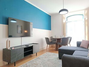 A modern living room with a TV mounted on the wall, a dining area with a table and chairs, and a sofa. - Sao Bento Tramview Residence (Lisboa)