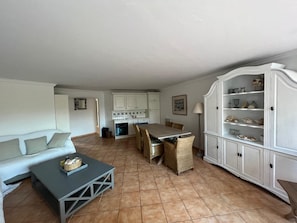 A spacious living area with a sofa, a dining table with chairs, a kitchen in the background, and a cabinet with shelves. - Family apartment 85m2 in gated community-Terrace-2 Pools-Tennis-Park (Cavalaire-sur-Mer)