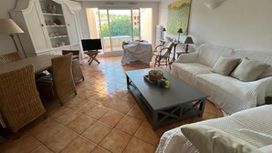 Un salón espacioso con un ventanal grande, un sofá blanco, una mesa de centro y un televisor.