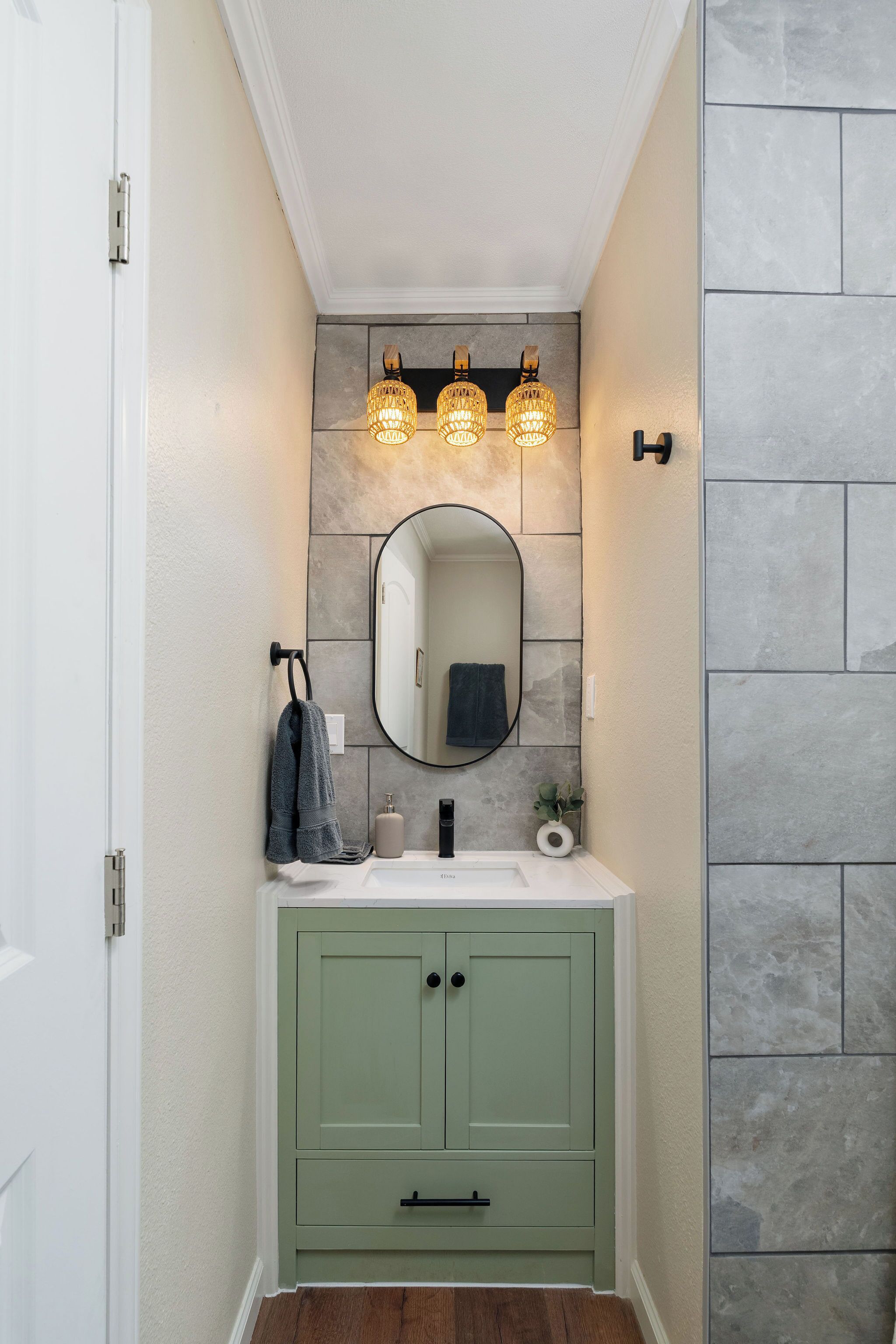 Une salle de bain avec un meuble-lavabo vert, un miroir rond et trois appliques murales.