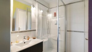 Un baño con ducha envuelta en vidrio, un lavamanos blanco y un espejo con iluminación.
