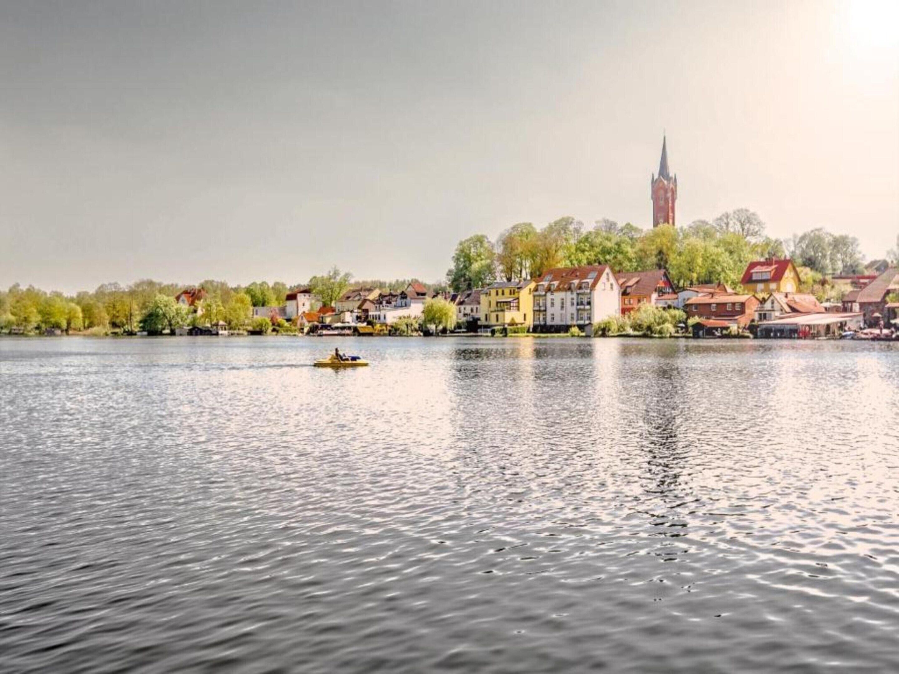 Un fiume tranquillo con una piccola barca, circondato da edifici colorati e da un campanile sullo sfondo.