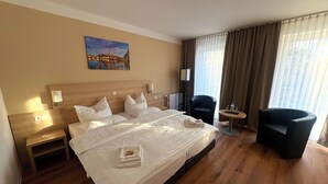 A hotel room with a large bed, a chair, a small table, a painting on the wall, and a window with curtains. - Kaiserhof Feldberg by Belvilla Resorts-family Room (Feldberger Seenlandschaft)