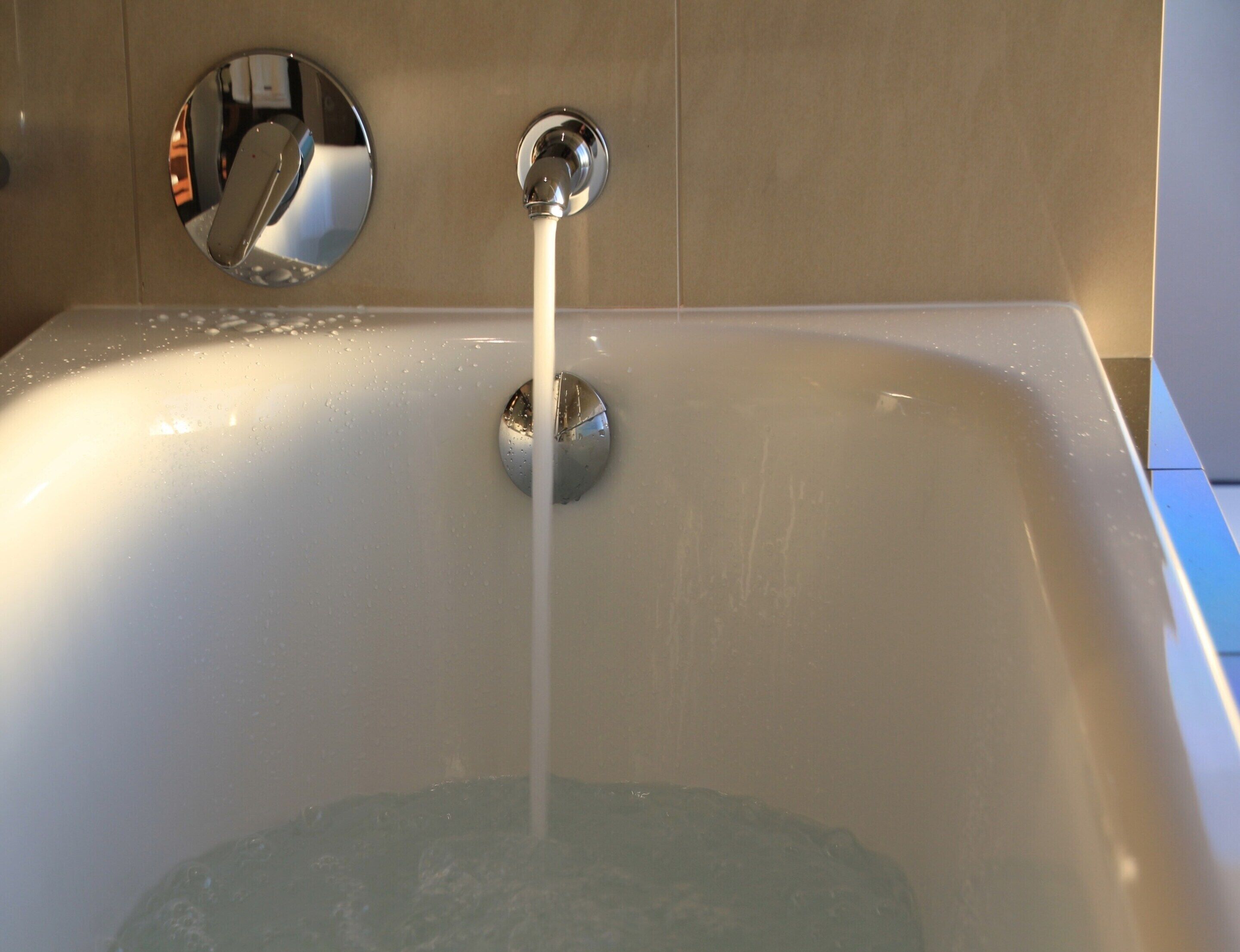 A bathtub with running water, a chrome faucet, and a round mirror on the wall.