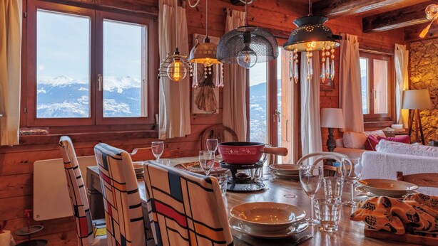 Uma cabana de madeira com área de jantar, apresentando uma mesa posta para quatro pessoas, cadeiras e luminárias pendentes.